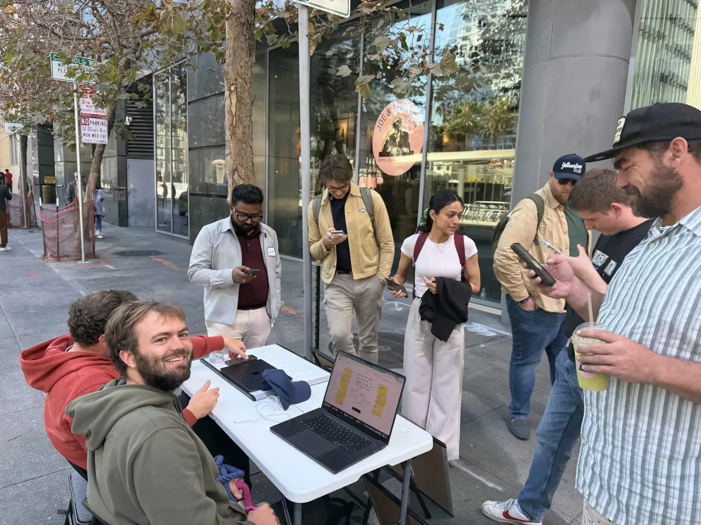People gathered around the stand looking at their phones, founders in olive and rust hoodies at the table.